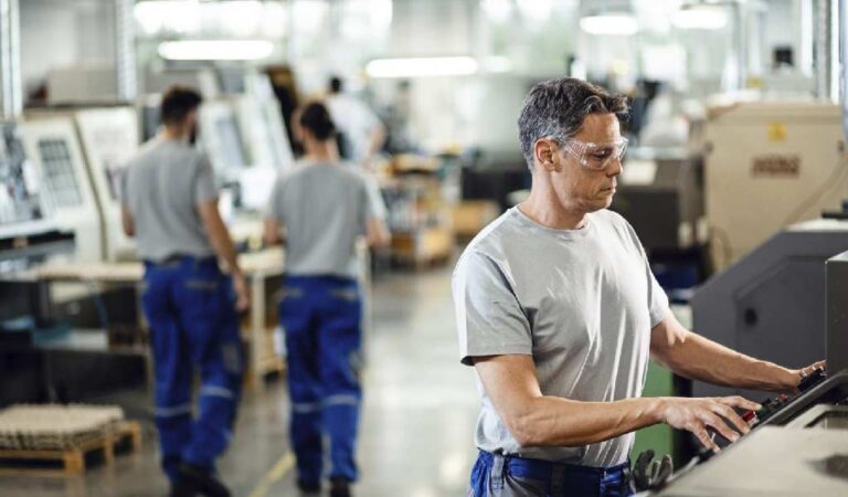 Taller industrial con máquinas cnc y varios trabajadores operando los controles de fabricación.